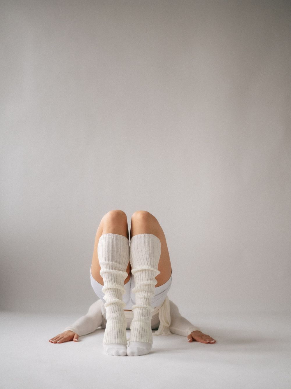Person sitting on floor wearing white knee-high socks and white outfit against a light gray background.