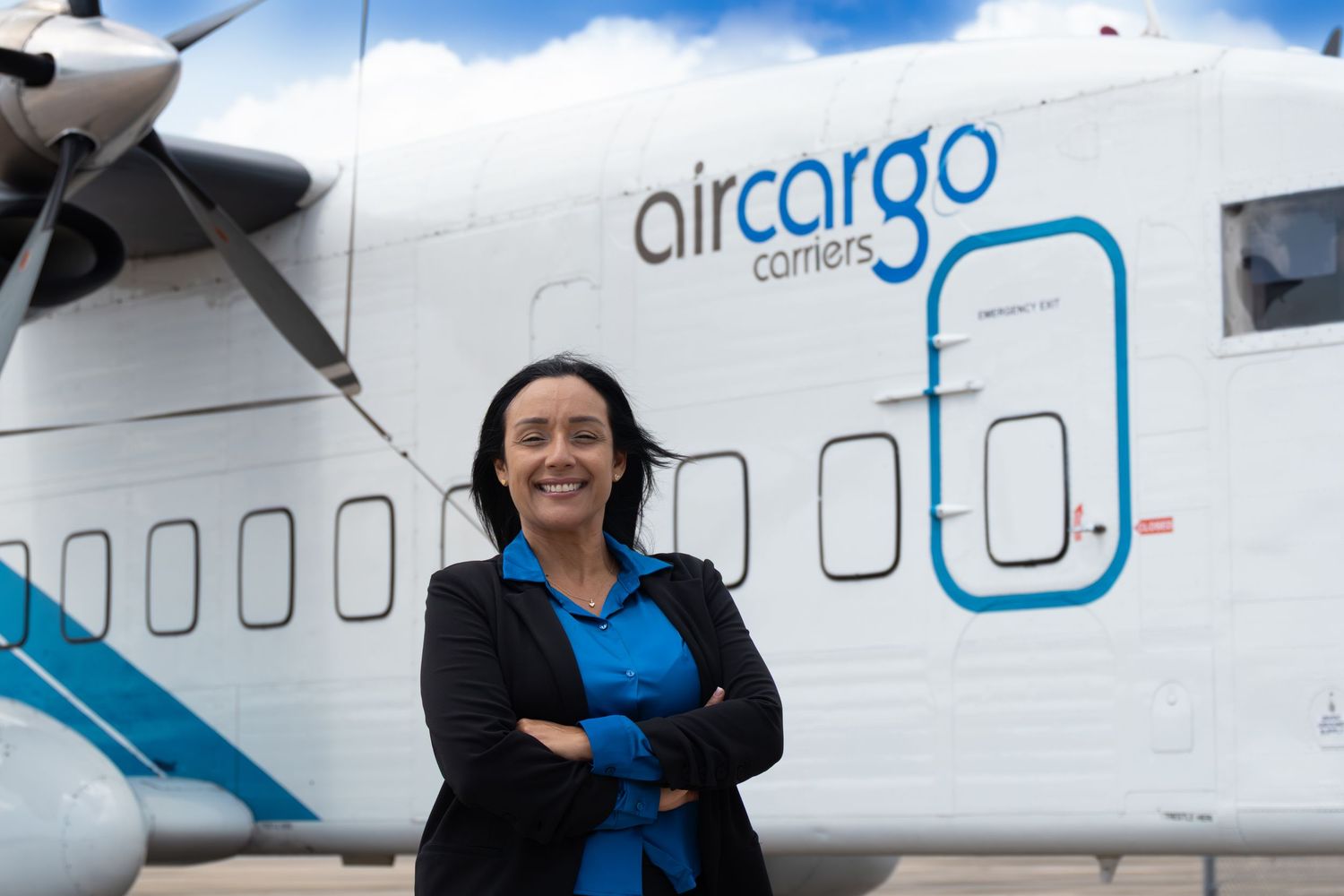 Woman standing in front of an Air Cargo turboprop aircraft on a tarmac under a partly cloudy sky.