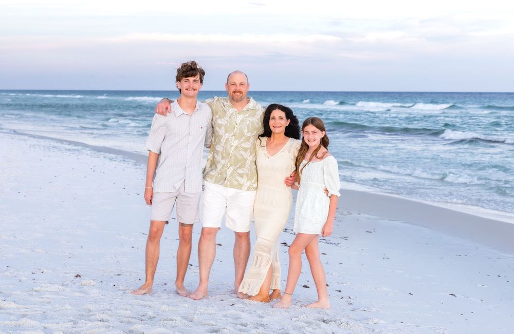 Family of four smiling together on a sandy beach with ocean waves in the background during golden hour.