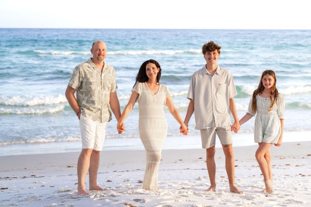 Happy family of four holding hands and smiling on a beautiful sandy beach with ocean waves.