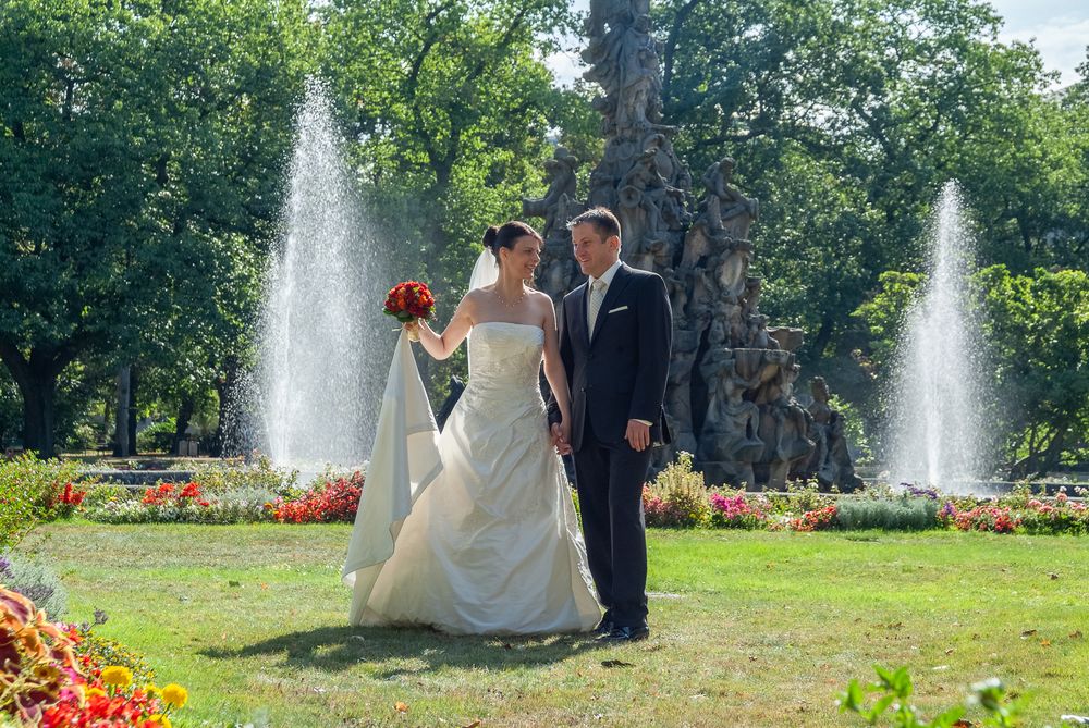 Braut und Bräutigam spazieren Hand in Hand vor den Springbrunnen im Erlanger Stadtpark. Natürliche Hochzeitsbilder im Freien.
