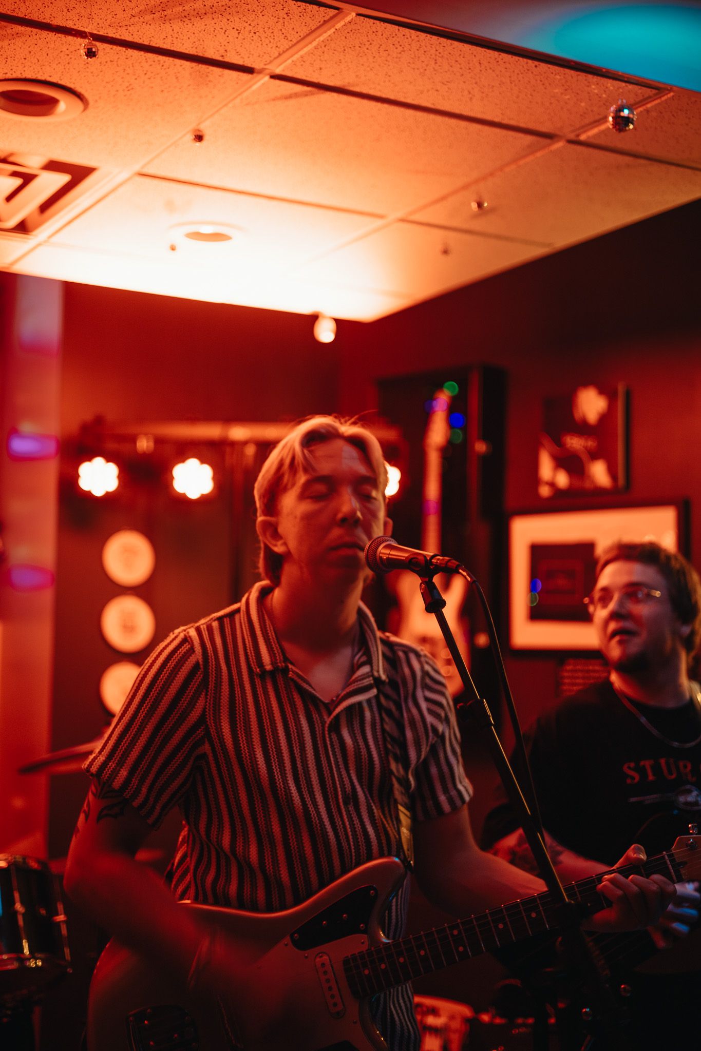 Band performing live on stage with guitars and drums in a warmly lit venue.