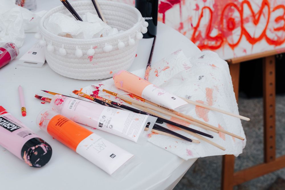 Art supplies including paint tubes and brushes scattered on a white table with a colorful LOVE graffiti backdrop.
