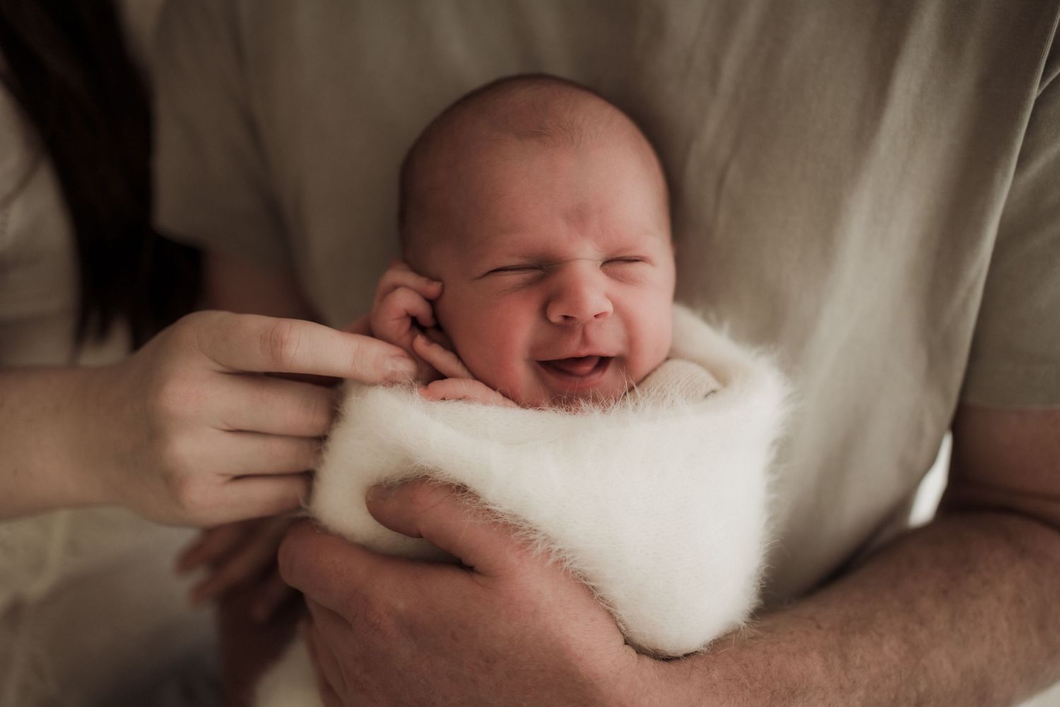 Newborn baby wrapped in white fluffy blanket smiling while being held by parents in Buxton, Victoria