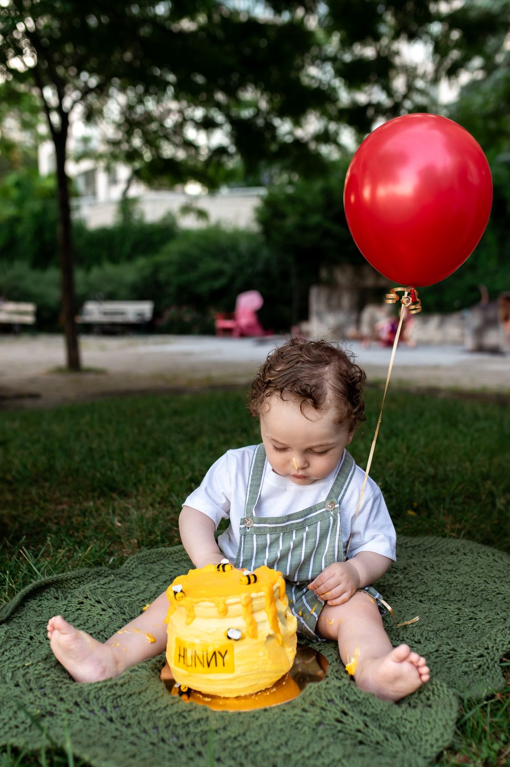 One year old baby boy sits on blanket with Winnie the Pooh Hunny pot smash cake and red balloon.