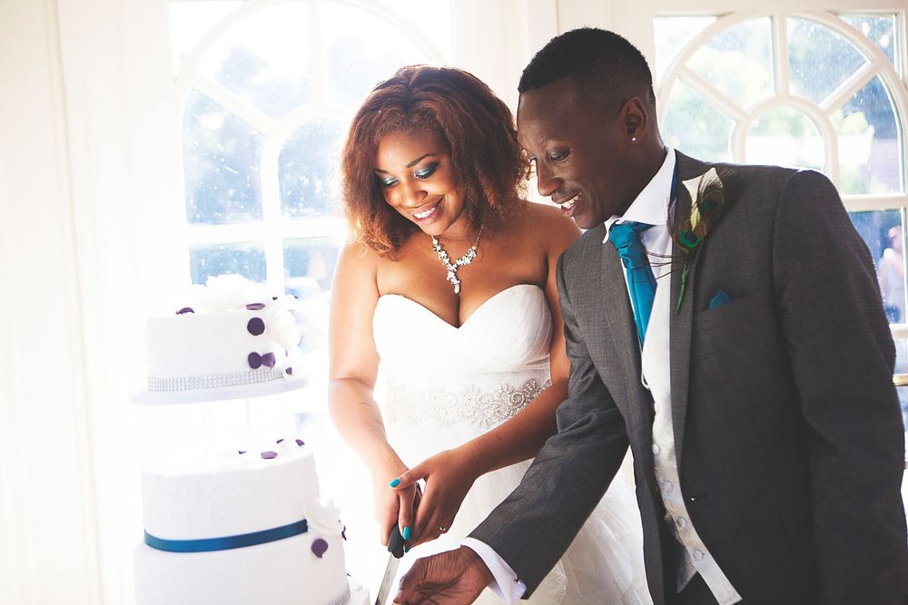 Bride and groom cutting their white wedding cake together, smiling joyfully at their elegant reception. At Oaks farm wedding venue in Surrey