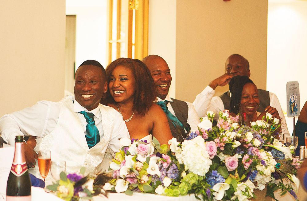 Happy wedding party guests laughing and smiling at a decorated reception table with floral arrangements and champagne. At Oaks farm wedding.