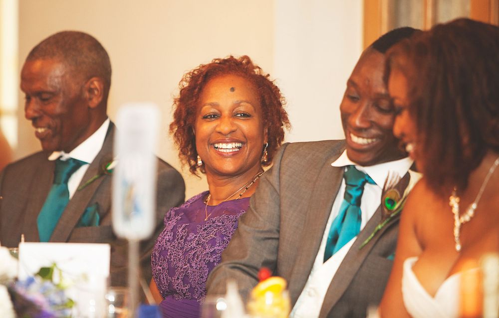 Family members in grey suits with teal ties laughing together at a joyful wedding reception celebration. At Oaks farm wedding venue.