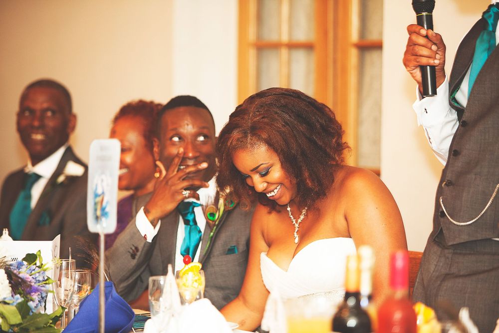 Bride and groom share a joyful moment during wedding reception speech, smiling at the head table. At Oaks farm wedding venue in Surrey.