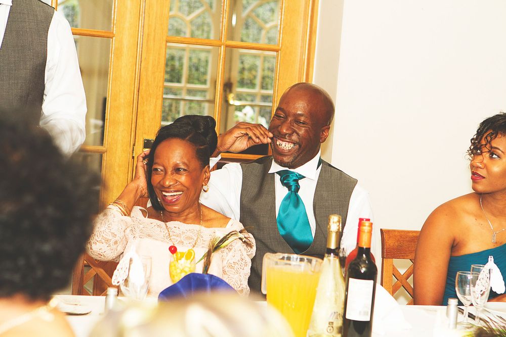 Couple smiling and laughing together at a wedding reception dinner table with drinks and guests nearby. At Oaks farm wedding venue in Surrey