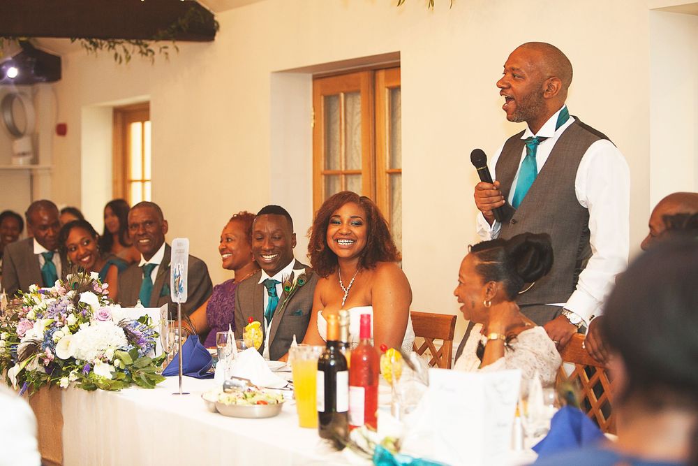 Best man delivers a heartfelt speech to laughing wedding guests at a elegant reception dinner. At Oaks farm wedding venue in Surrey.