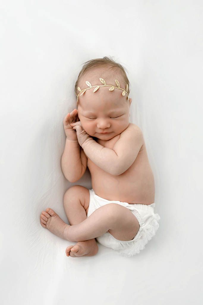 Peaceful newborn baby girl sleeping on white fur wearing a delicate gold leaf headband.