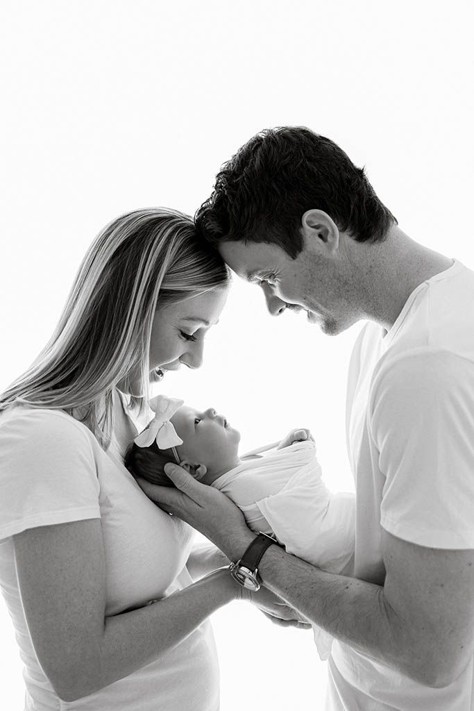 Black and white photo of parents lovingly gazing at their newborn baby, cradling the infant together.
