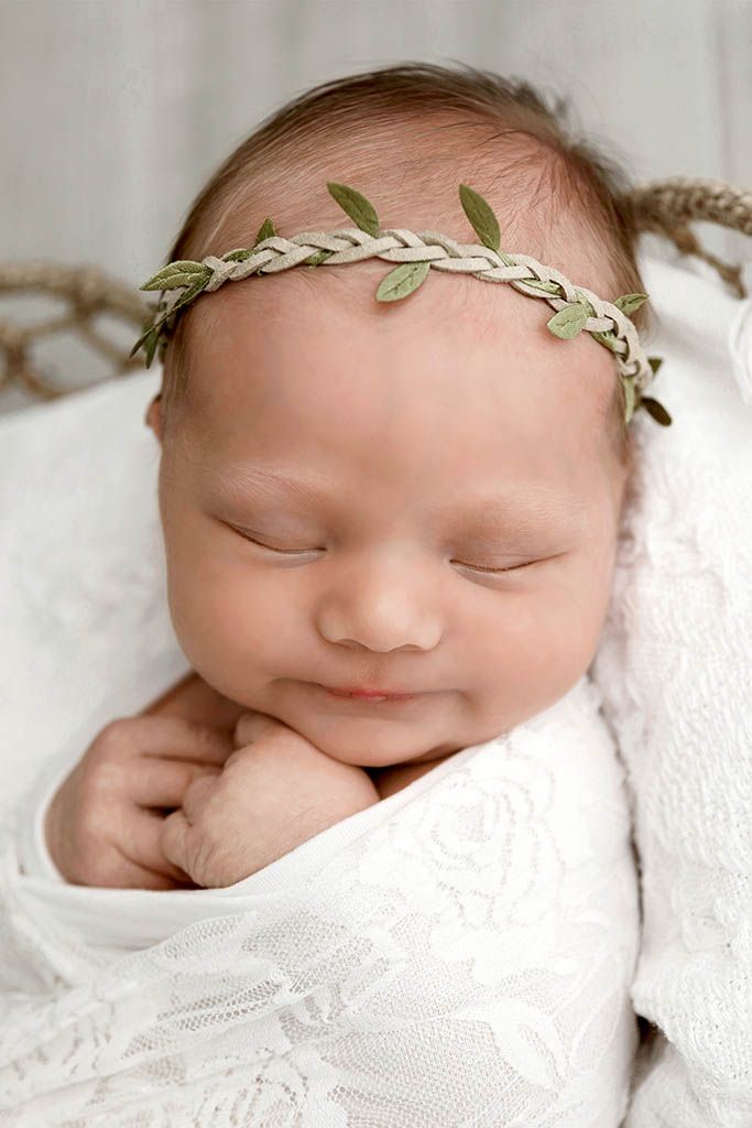 Serene newborn baby sleeping wrapped in white lace with delicate green leaf crown headband.