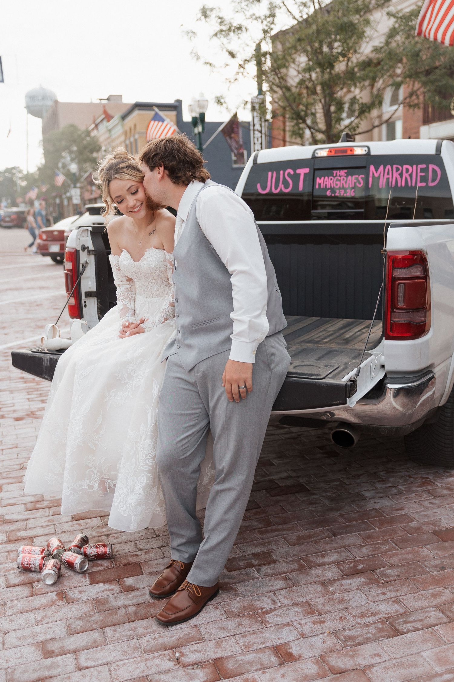 Newlywed couple sharing a kiss on a truck tailgate with Just Married sign on their wedding day.