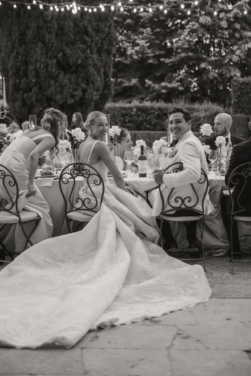 Black and white photo of bride and groom smiling at outdoor wedding reception dinner table.