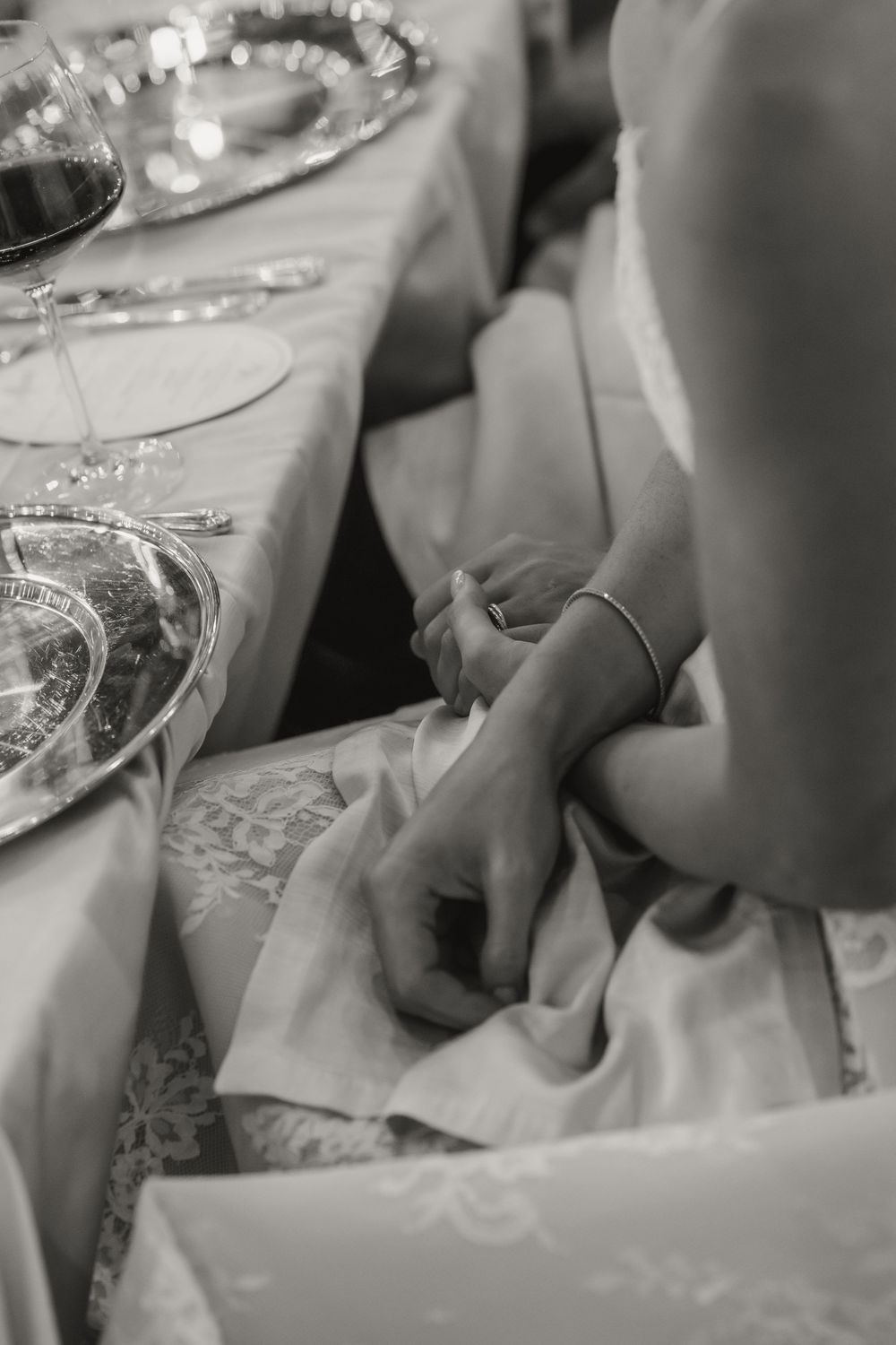 Close-up black and white photo of bride nervously fidgeting with napkin at elegant wedding reception table.