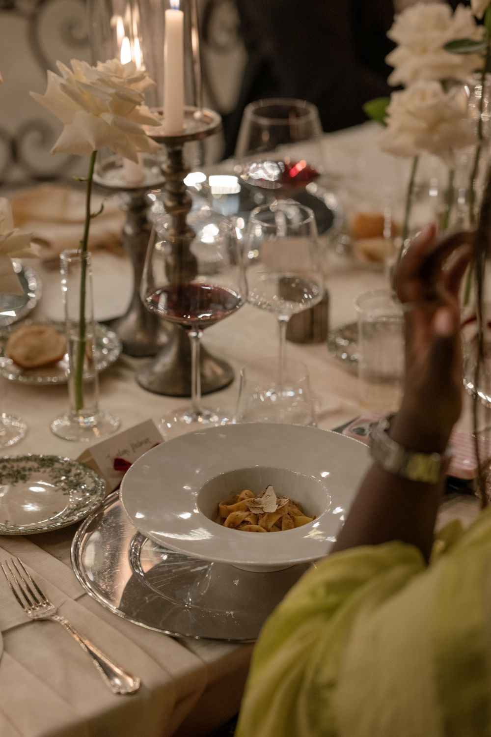 Elegant wedding reception table with candlelight, white roses, crystal glasses, and a pasta dish on fine china.