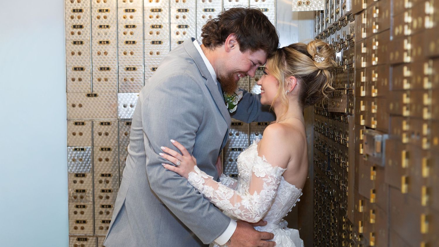 Bride and groom share a romantic kiss in front of vintage gold safe deposit boxes at a unique wedding venue.