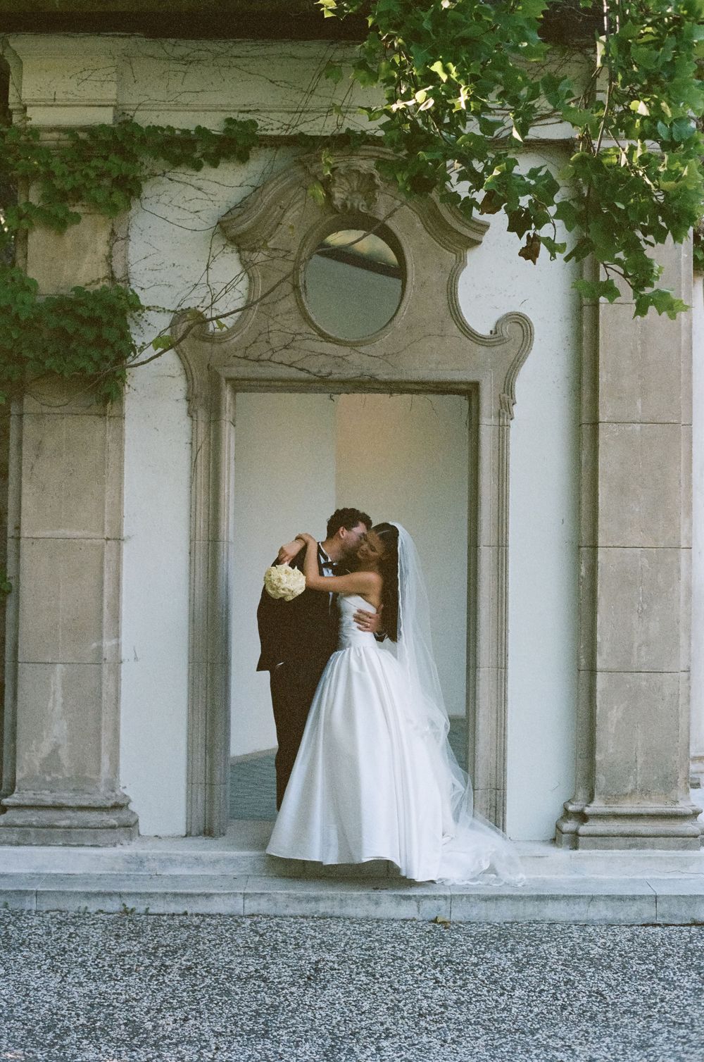 Bride and groom share a romantic kiss in a white strapless gown at an ornate stone doorway.