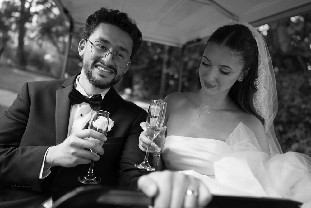 Black and white photo of a smiling bride and groom toasting with champagne glasses at their wedding reception.