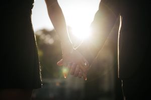 Two people holding hands backlit by golden sunlight in a romantic silhouette engagement photo.