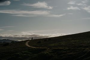 Winding dirt path through dark rolling hills under a dramatic cloudy sky at dusk.