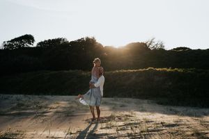 Couple dancing in golden sunset light on sandy beach surrounded by coastal dune vegetation.