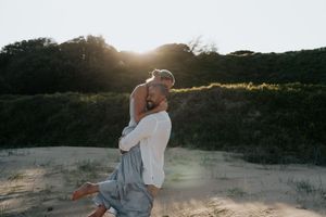 Man lifting woman in his arms on sandy beach with warm golden sunset backlight.