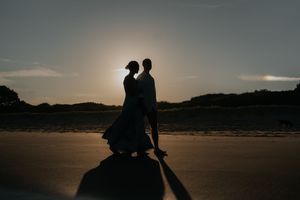 Romantic silhouette of couple dancing on beach at sunset with long shadows cast behind.