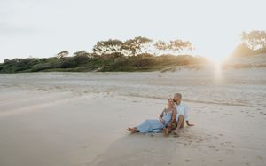 Couple relaxing together on wide sandy beach at warm golden sunset.