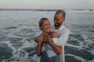 Smiling couple embracing in shallow ocean waves at sunset on beach.