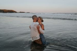 Romantic couple kissing in shallow ocean water at dusk on beach.