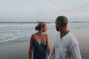 Couple walking hand in hand along shoreline at dusk on beach.