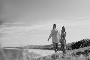 Black and white photo of couple walking hand in hand along a scenic coastal path.