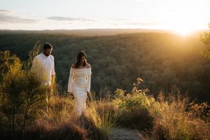 Couple walking hand in hand through golden wildflowers during a stunning sunset engagement shoot.