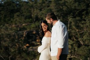Couple smiling and embracing during a romantic outdoor engagement session in natural bushland.