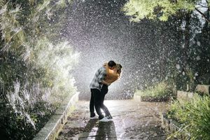 Couple embracing romantically in the rain on a tree-lined path at night.