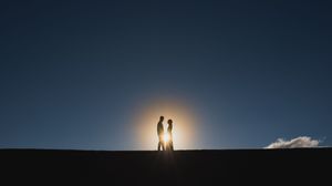 Couple silhouetted against a glowing sunset on a hilltop.