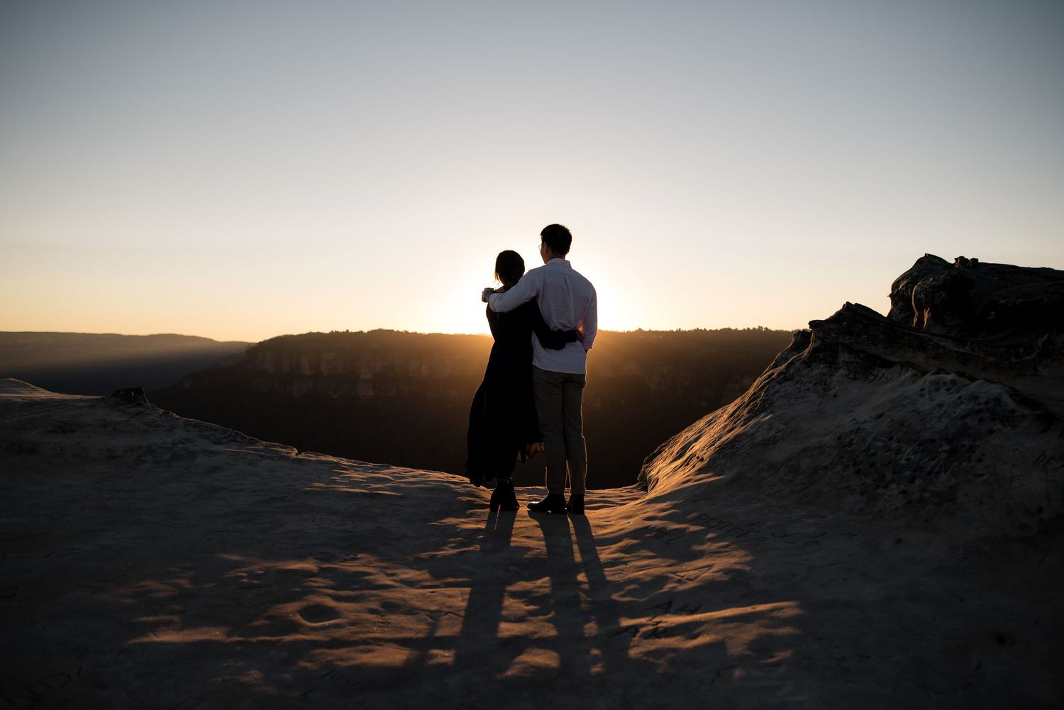 Couple watching a golden sunset from a rocky desert hilltop.