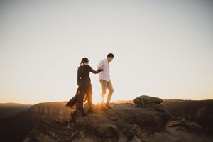 Couple holding hands walking on rocky mountain at golden sunset.