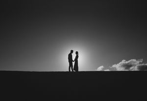 Silhouette of couple holding hands against glowing sunset sky.