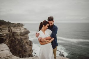 Couple embracing on a coastal cliff with ocean views.