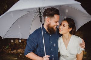 Couple sharing a romantic moment under a white umbrella in the rain.