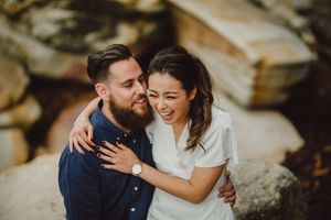 Couple laughing and embracing outdoors near rocky terrain.