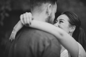 Black and white photo of woman smiling while embracing man outdoors.
