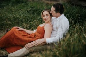 Couple sitting together in tall green grass, sharing a peaceful and romantic embrace.