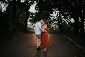 Couple embracing on a quiet tree-lined road in soft evening light.