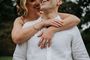 Joyful couple embracing closely, woman wearing a blue sapphire ring and gold bracelet.
