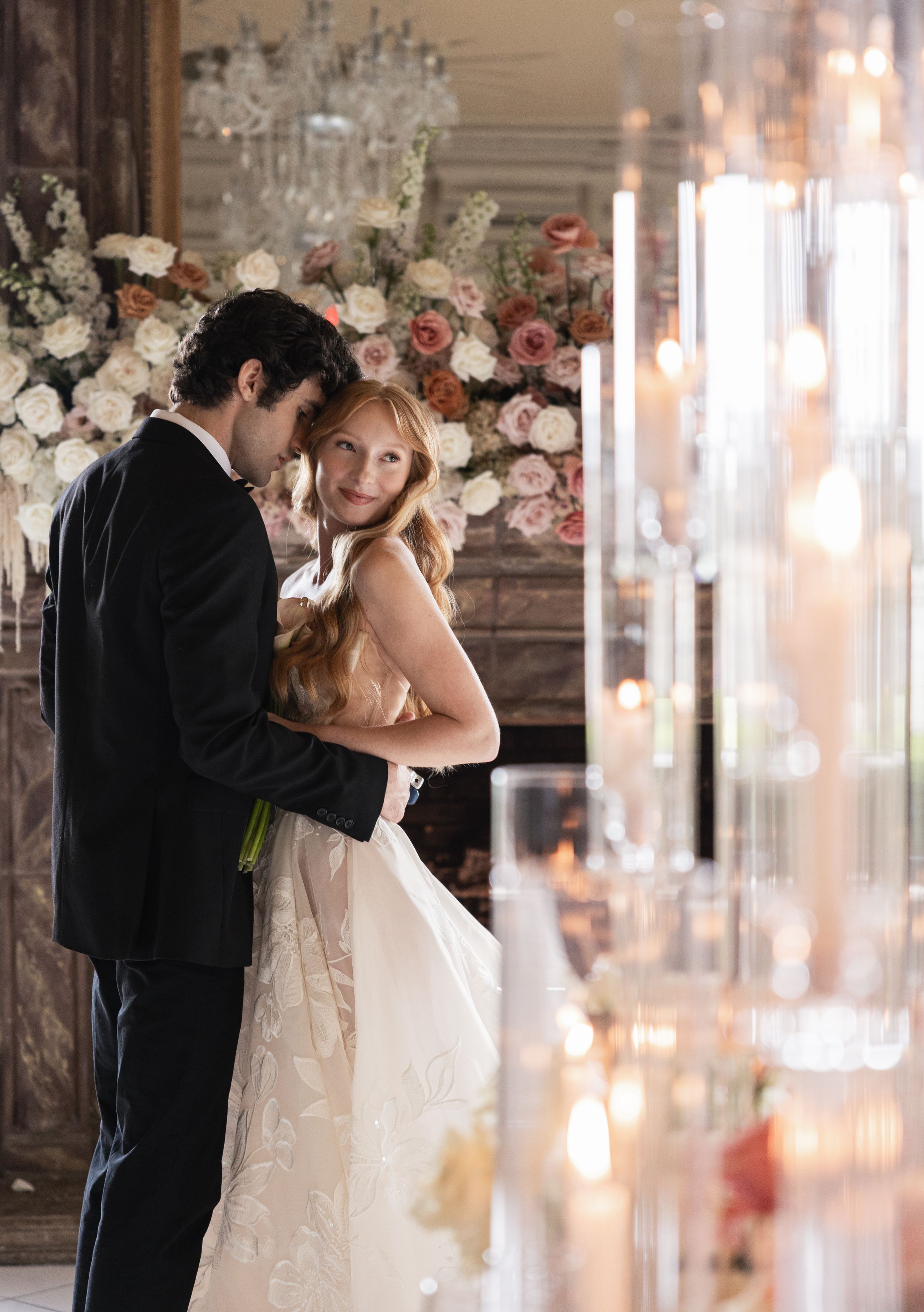 Elegant bride and groom share a romantic moment surrounded by candles and floral arrangements at a wedding reception.